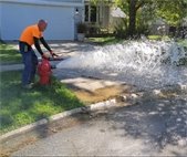 A photo of a City worker flushing a fire hydrant. 